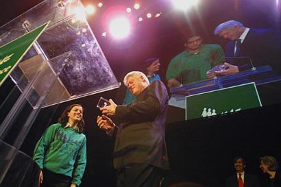 Former President Bill Clinton, center, accepts a gift from 17 year-old Hilla Meller, left, from Haifa, Israel during the 'Seeds of Peace Celebrity Auction' Tuesday, Jan. 14, 2003 in New York. Since 1993, Seeds has brought together about 2,000 youths from warring lands, Israelis and Palestinians, Indians and Pakistanis, Cypriot Turks and Greeks, Bosnian Muslims and Serbs, and tribal members from Afghanistan. Twenty year-old Palestinian Adham Rishmawi, stands next to Clinton in monitor. Photo by Tina Fineberg