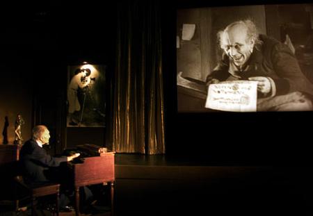 Bob Mitchell, left, demonstrates how he plays the organ during silent movies such as 'Nosferatu,' shown on the screen at right, at the Silent Movie Theater in the Hollywood section of Los Angeles Tuesday, Oct. 8, 2002. Mitchell, who began playing the organ for silent films in 1924, believed to be the last remaining organist from the silent-movie era, still plays one or two nights each weekend at the theater. Photo by Jean-Marc Bouju