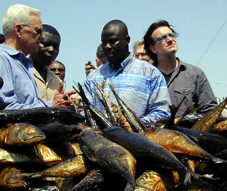 Treasury Secretary Paul O'Neill (L) and U2 frontman Bono (R) visit a women's community fish smoking project in Ghana's capital of Accra, May 22, 2002. Photo by David Clarke