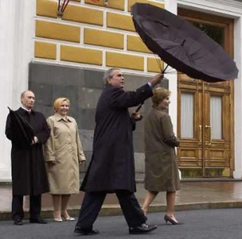 Russian President Vladimir Putin (L) and his wife Lyudmila (2nd L) watch U.S. resident George W. Bush holds his umbrella in the wind and U.S. first lady Laura (R) walks by on their arrival for the military parade in Moscow, May 9, 2005. Russian military and veterans paraded in Red Square in a victory ceremony watched by U.S. resident George W. Bush and other leaders.