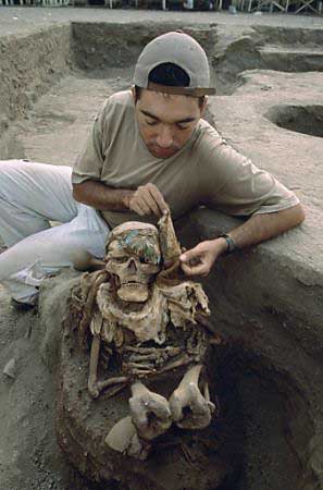 Swathed in cloth and cotton seeds, a mummy of an Inca man unearthed at Puruchuco, Peru, retains the headdress feathers that marked him as an individual of high Inca rank. Excavation team member Antonio Gamonal helps remove a mantle that covered the mummy's face. Photo by Ira Block/National Geographic Society