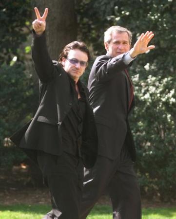 Bono, left, gives the peace sign as he walks to the White House from the Inter-American Development Bank, Thursday, March 14, 2002, where Bush spoke. Photo by Ron Edmonds