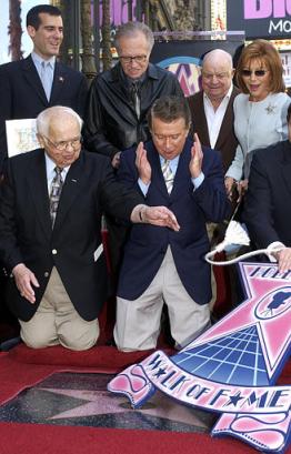 Talk show host Regis Philbin, bottom center, reacts as honorary Mayor of Hollywood Johnny Grant, lower left, presents a star to him on the Hollywood Walk of Fame Thursday, April 10, 2003, in Los Angeles. Watching Philbin are Los Angeles City Councilman Eric Garcetti, top left, talk show host Larry King, second left, comedian Don Rickles and Philbin's wife Joy, top right. Photo by Nick Ut